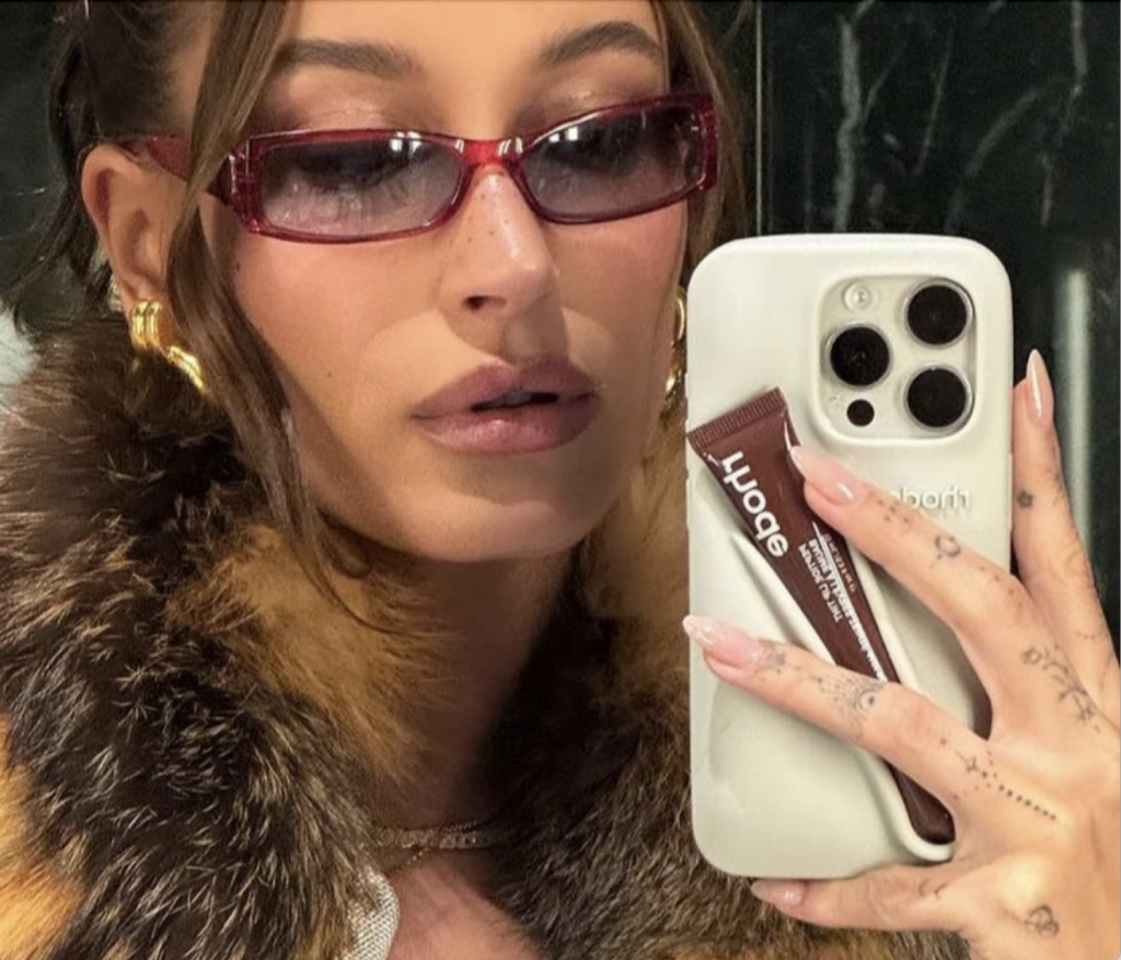 Hailey Bieber holding Rhode Skin phone case with a lip balm holder