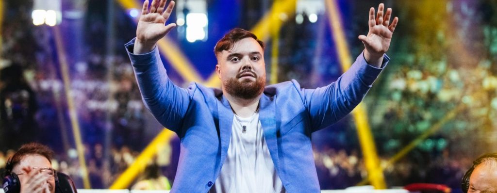 Ibai surrounded by lights and dressed in a blue suit and white t-shirt facing the public with his hands up.